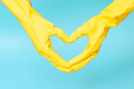 Hands in yellow rubber gloves in the shape of a heart on a blue backgroundの写真素材