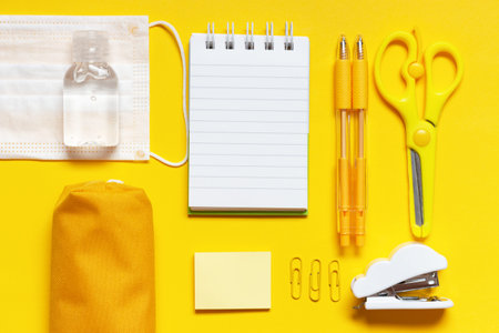 Stationery, notepad and medical mask on a yellow background top view, copy space