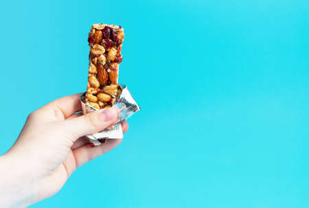 A woman's hand holds a cereal bar on a blue background, a copy of the spaceの写真素材