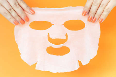 Women's hands with manicure hold a moisturizing face mask on an orange backgroundの写真素材