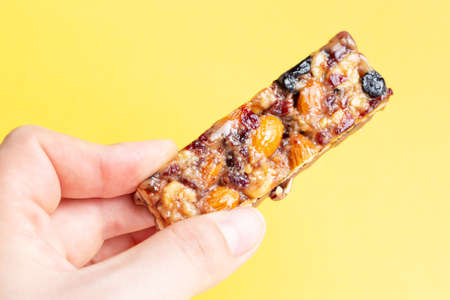 A woman's hand holds a cereal bar on a yellow backgroundの写真素材
