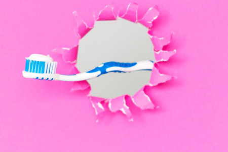 Toothbrush with toothpaste on pink background on a torn pink paper background