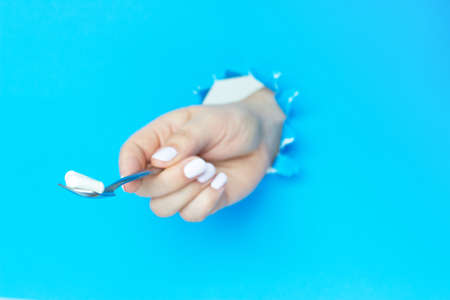 A woman's hand holds a spoon with a tablet on a blue background, a copy of the spaceの写真素材