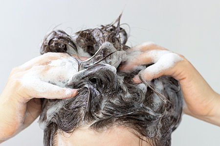 A girl washes her hair with shampoo on a white background, front view