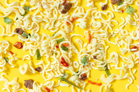 Dry noodles with spices broken down lies on a yellow background