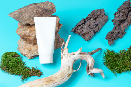 White tube of cream lies on a stone near a wooden branch on a blue backgroundの写真素材