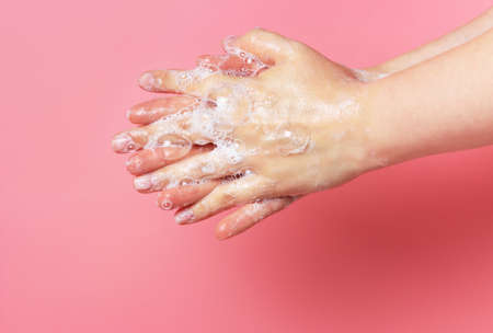 The girl washes her hands with soap and foam on pink backgroundの写真素材