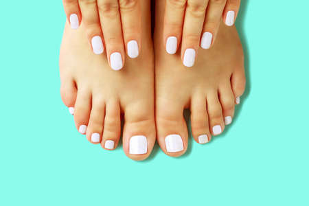 Female hands with white manicure and pedicure on blue background, top viewの写真素材