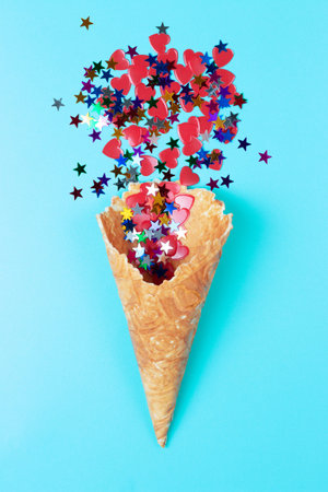 Waffle horn and multicolored confetti on blue background, top view