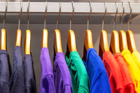 Bright multicolored T-shirts hang on wooden hangers in the store.の写真素材