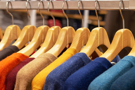 Multicolored knitted sweaters hang on wooden hangers, autumn modern clothesの写真素材
