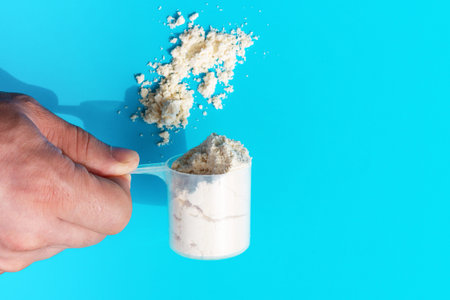 Male hand holds a measuring spoon with protein on blue background top view.
