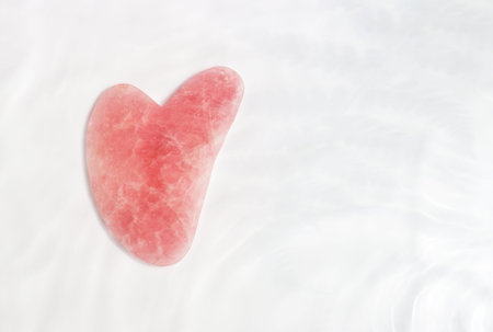 Quartz pink gua sha underwater and a shadows, top view copy space