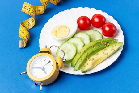 Plate with salad, alarm clock and measuring tape on blue backgroundの写真素材