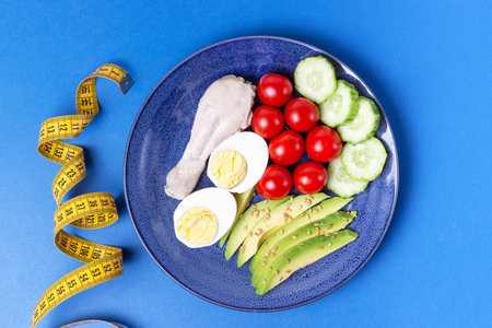 Plate with vegetables and yellow tape measure on a blue background