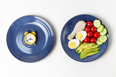 Two plates with food and alarm clock on a white background, Interval fasting concept.