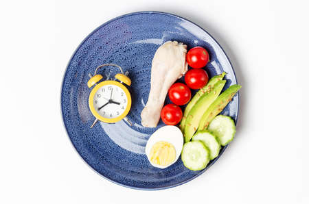 Plate with vegetables and alarm clock on white background, intermittent fasting concept.の写真素材