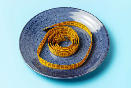 Yellow tape measure in a plate on a blue background, concept of diet.の写真素材