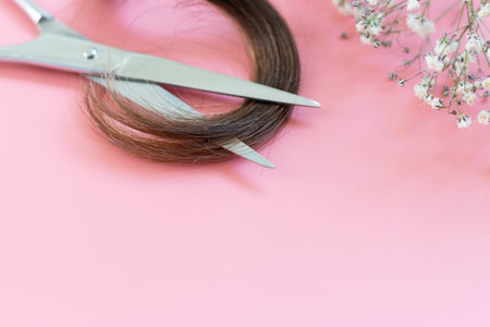 Scissors and strand of split ends of hair on pink background