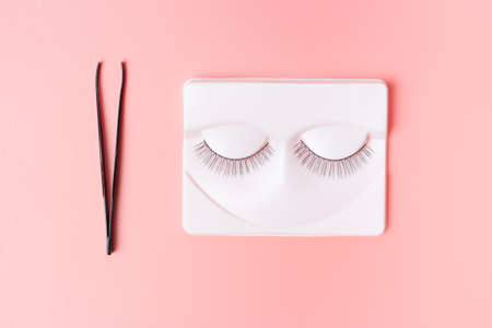 Black false eyelashes and tweezers on a pink background, view from aboveの写真素材