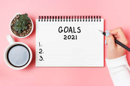 Female hand writes in notepad of goals 2021 on pink background, top viewの写真素材