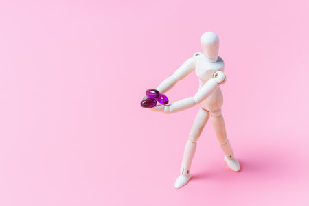 Pills and capsules in wooden hand on pink background.の写真素材