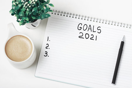 Notepad with inscription goals 2021 and cup of coffee on white background.