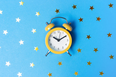 Alarm clock and confetti in shape of the stars on blue background top view.の写真素材