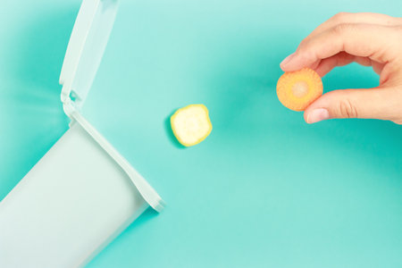 Female hand throws food waste into a plastic trash can on blue background.の写真素材