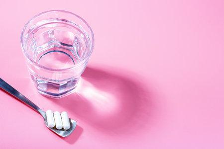 Glass of water and collagen capsules on pink background, copy space.の写真素材