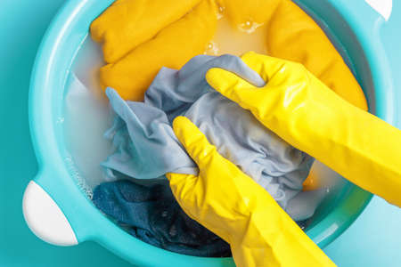 Female hands in rubber gloves washing blue clothes in basin, top viewの写真素材