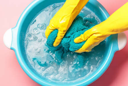 Female hands in rubber gloves washing blue towel in basin, top viewの写真素材