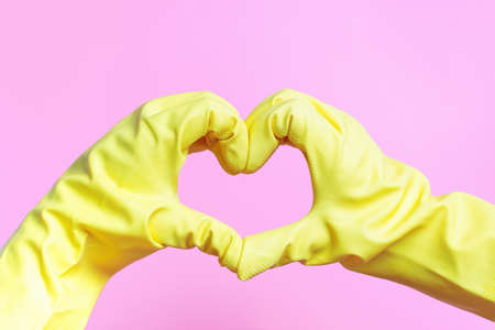 Hands in yellow rubber gloves in the shape of heart on pink backgroundの写真素材