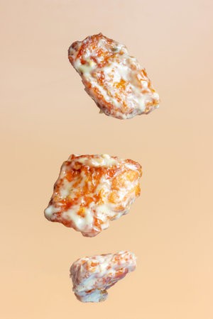 Cooked chicken pieces with sauce levitate on brown background.