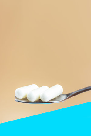 White collagen capsules in teaspoon close-up on a blue and brown background