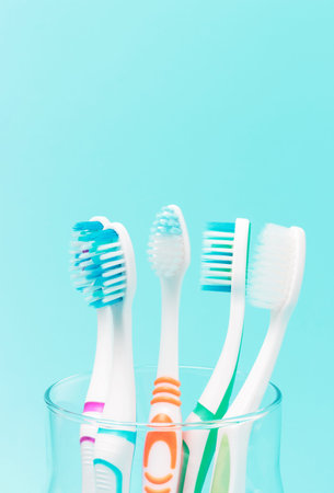 Multi-colored toothbrushes in a glass cup on blue background