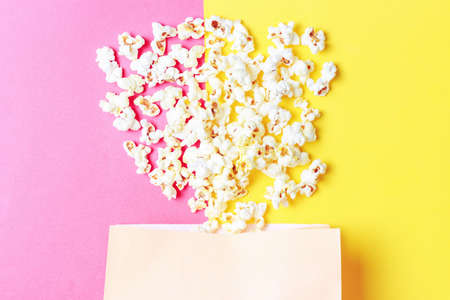 Package with sprinkled popcorn on pink and yellow background close-up.の写真素材