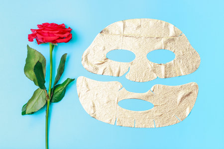 Gold fabric mask and rose on blue background close-up.の写真素材