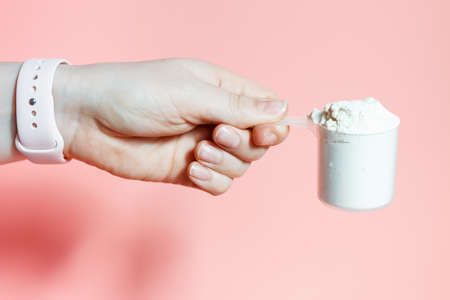 The woman's hand holds the protein in scoop on a pink background.の写真素材