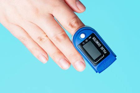 The pulse oximeter on a female hand on blue background close-up.
