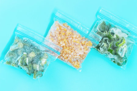 Three packages with frozen vegetables on blue background, top view.の写真素材