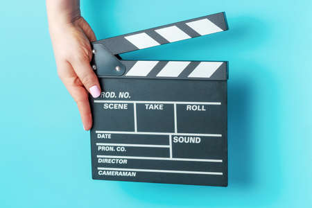 Female hand holding movie clapper board close-up on blue background.の写真素材