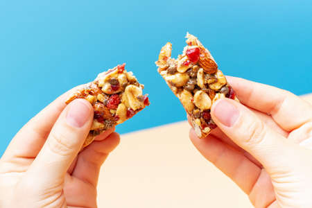 Female hands holding broken piece of protein bar on blue and brown background.の写真素材