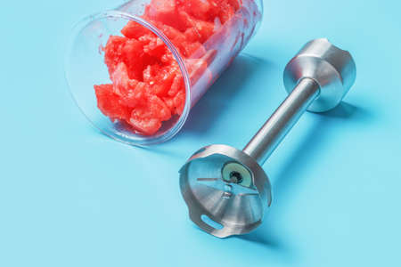 Hand blender and bowl with watermelon on blue background close-up.の写真素材