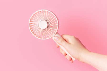 Female hand holding a small fan on pink background close-up.の写真素材