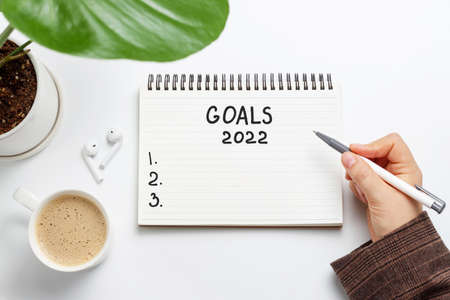 Female hand writes in notepad of goals 2022 on white background, top viewの写真素材