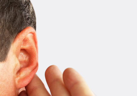 Man put his hand to his ear and listens close-up on white background.