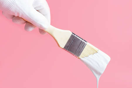 Hand in glove holds paintbrush with paint on pink background, repair concept.の写真素材
