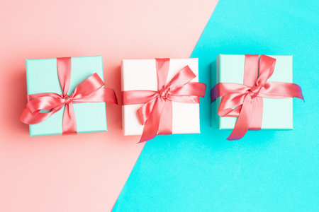 Three gift boxes with ribbons on pink and blue background close-up, top view