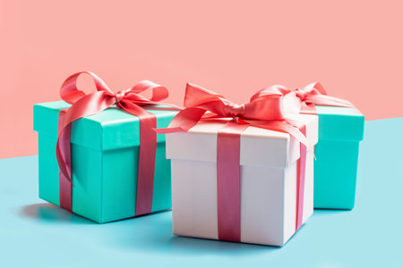 Three gift boxes with ribbons on pink and blue background close-up, front view
